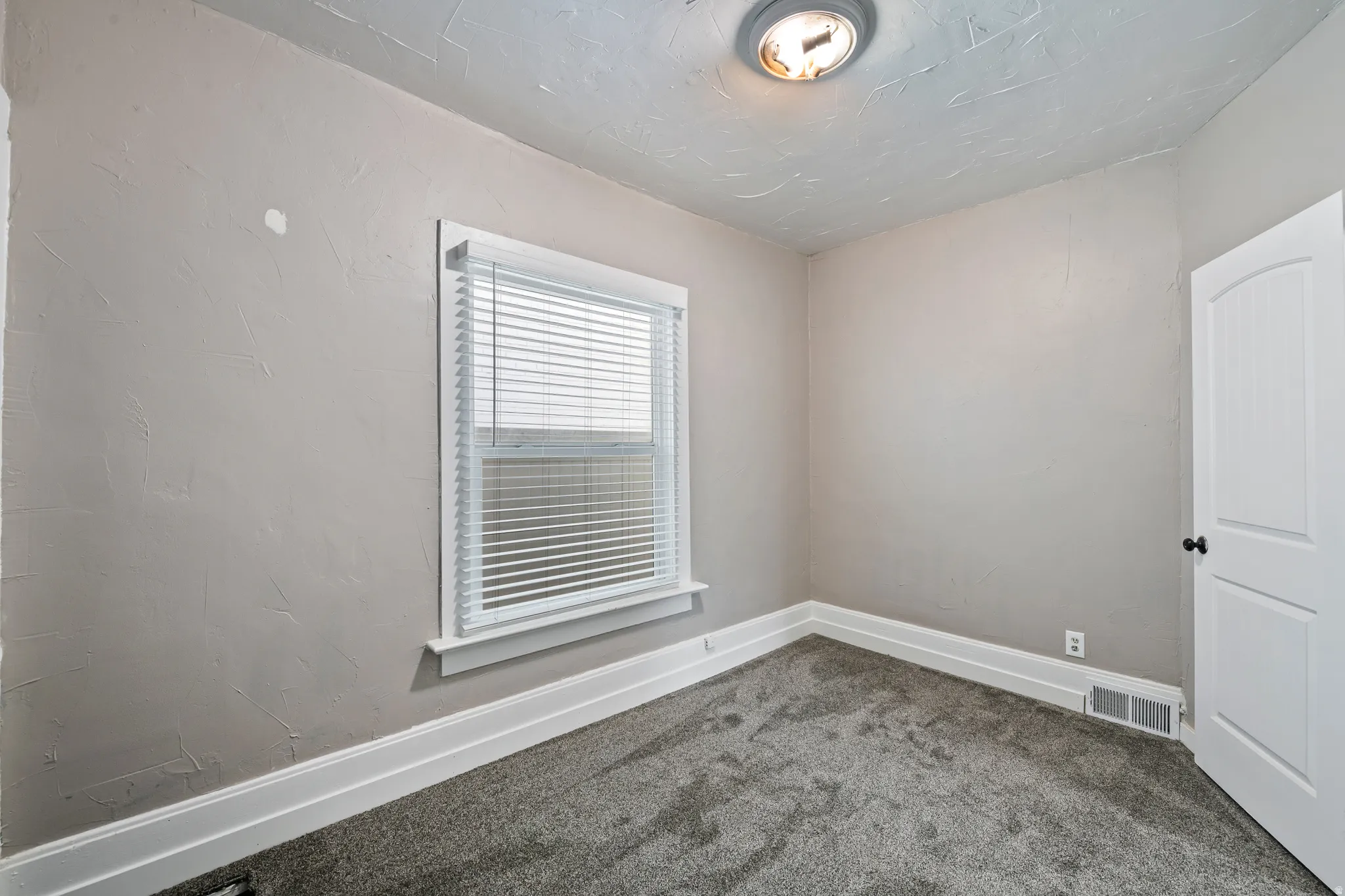 Neutral tone wall finish with a single window featuring white blinds and trim