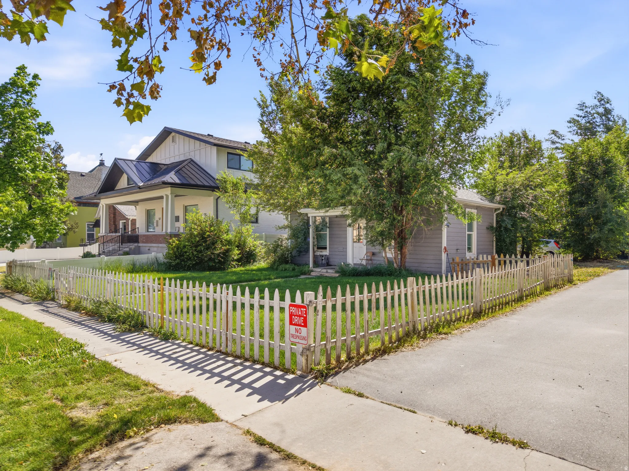 Corner lot residence featuring a white picket fence, a manicured lawn, and mature trees
