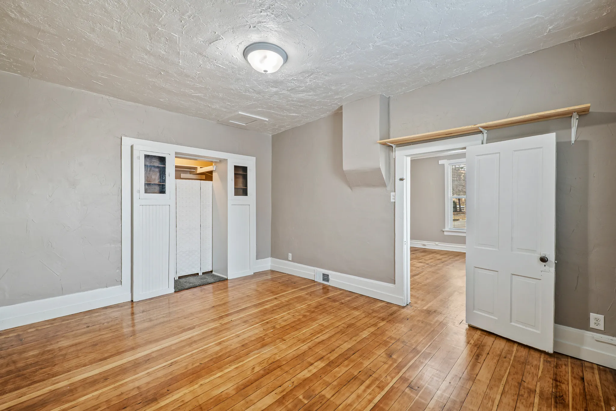 Hardwood flooring throughout, neutral painted walls, white trim, recessed entry with paneled doors, and a ceiling-mounted light fixture
