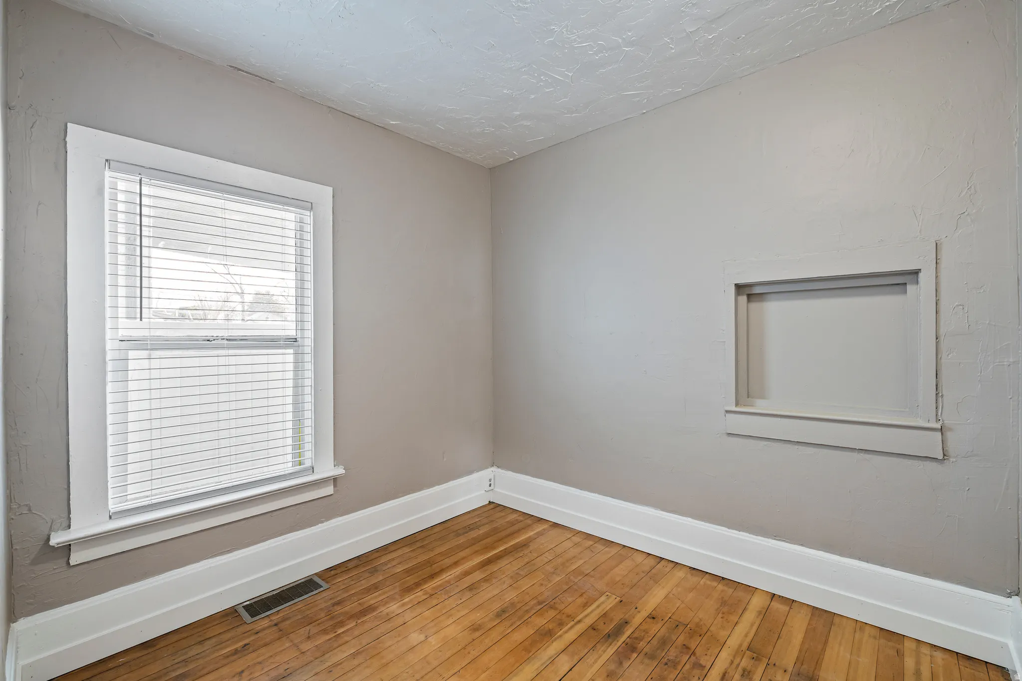 Interior room featuring wood-finish flooring, a double-hung window with blinds, and a built-in wall niche