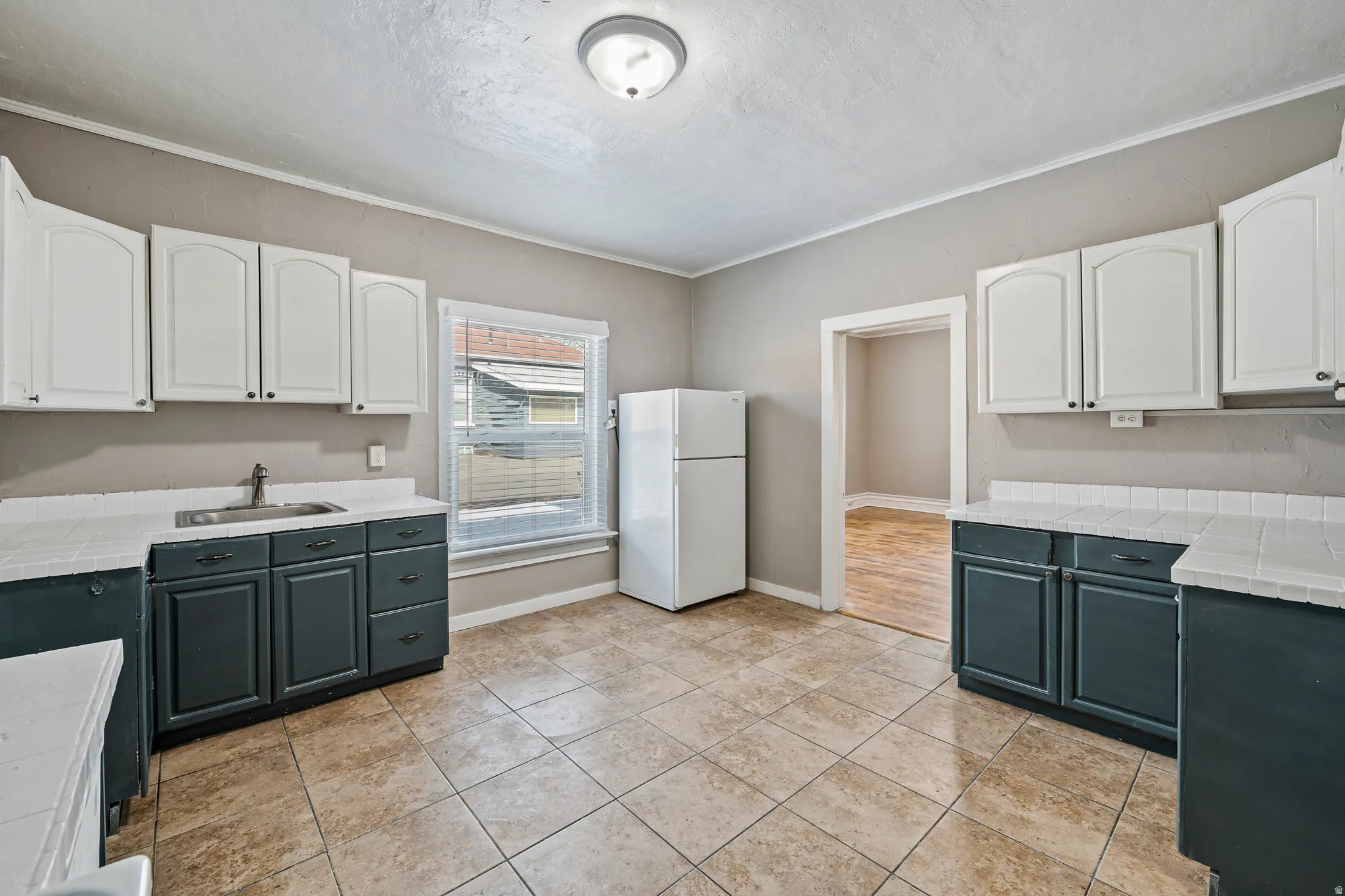 Kitchen featuring white upper cabinetry, dark lower cabinetry, tile flooring, and a white refrigerator