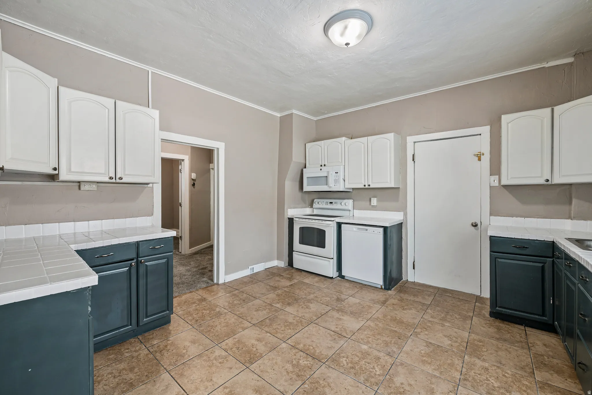 Kitchen featuring tiled flooring, two-tone cabinetry with white upper and dark lower cabinets, a white tile backsplash, and a white appliance suite including a range, microwave, and dishwasher