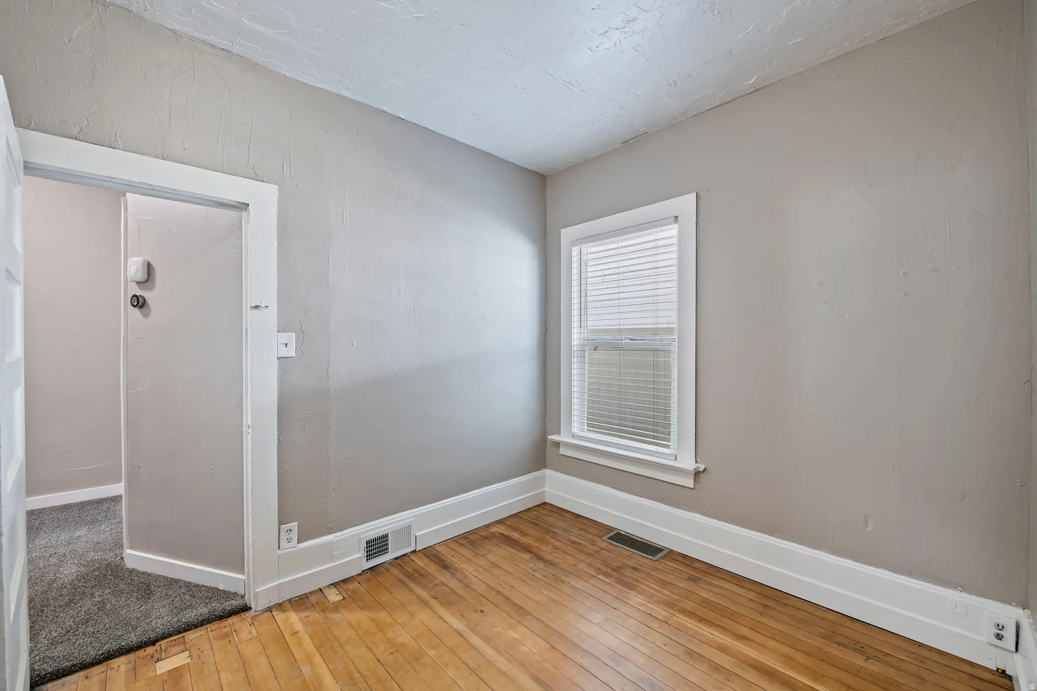 Room featuring hardwood flooring, white trim, a single window with blinds, and light-toned wall paint