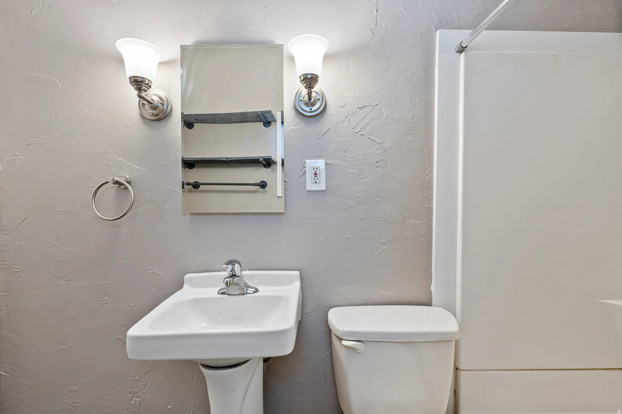 Pedestal sink with chrome faucet, flanked by a wall-mounted medicine cabinet with integrated shelving and dual sconce lighting