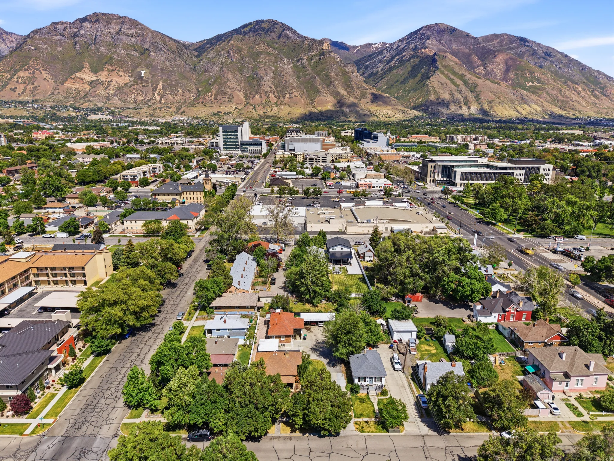 Expansive aerial perspective showcasing a developed urban area with varied architectural styles, mature trees, and mountainous terrain in the background