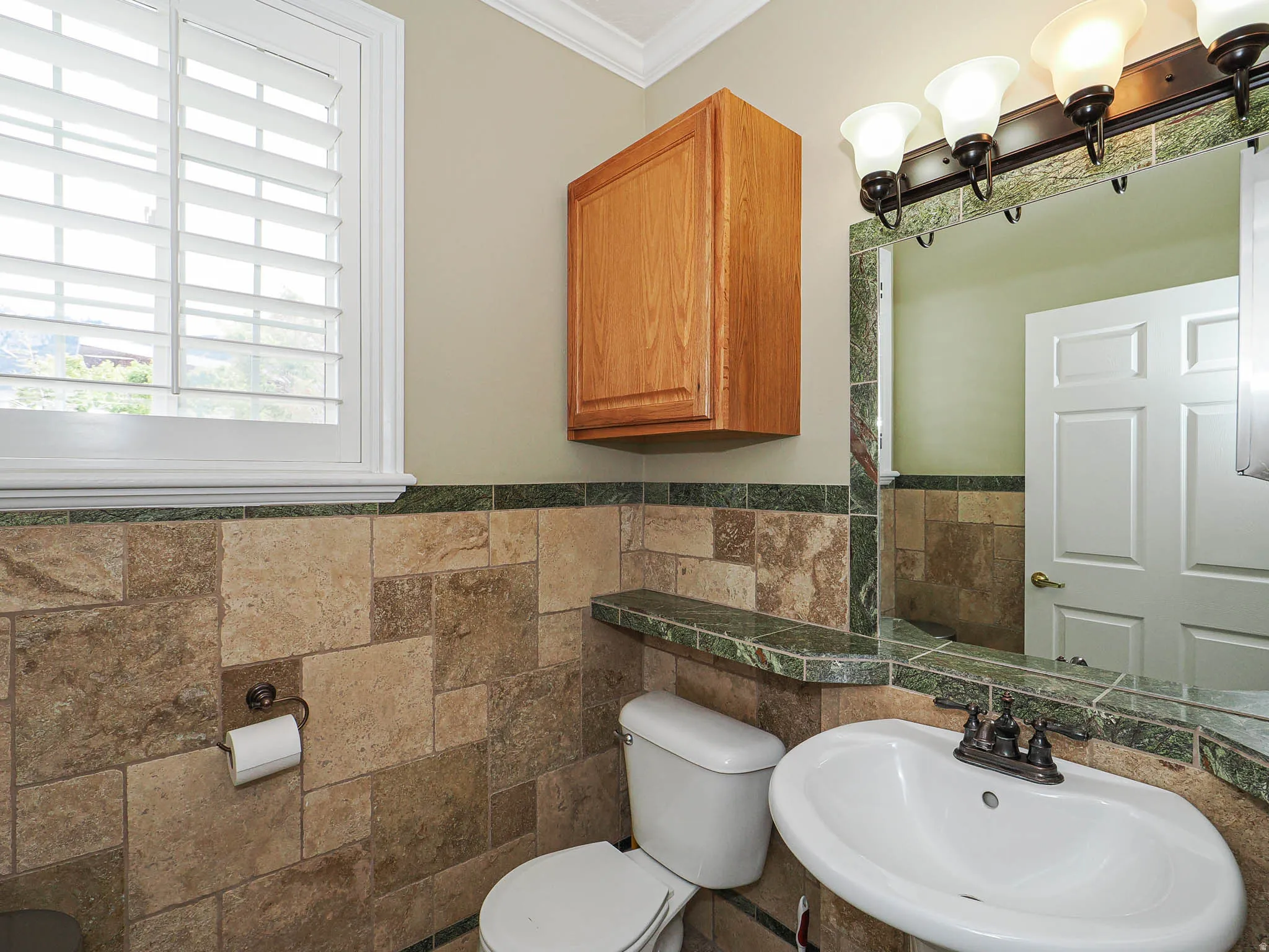 Bathroom featuring crown molding, tile walls, and a wainscoted wall