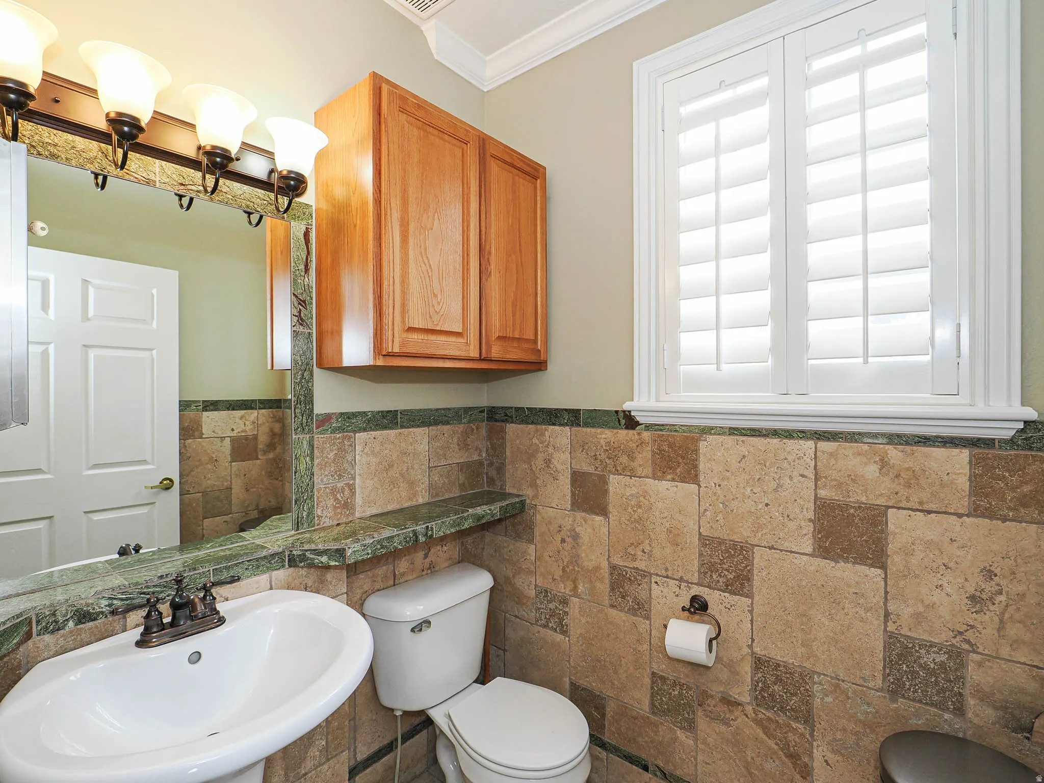 Half bathroom with ornamental molding, a wainscoted wall, and tile walls