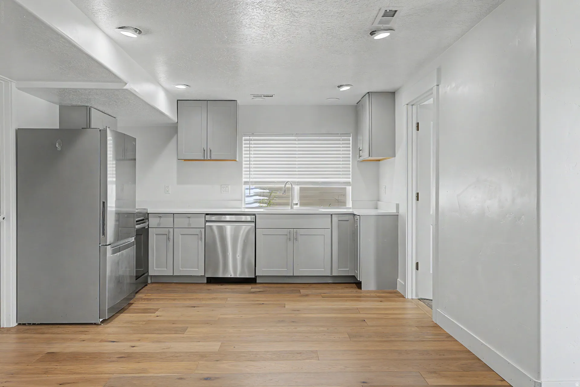 Basement Modern kitchen featuring light gray cabinetry, stainless steel appliances, white countertops, and wood-finish flooring