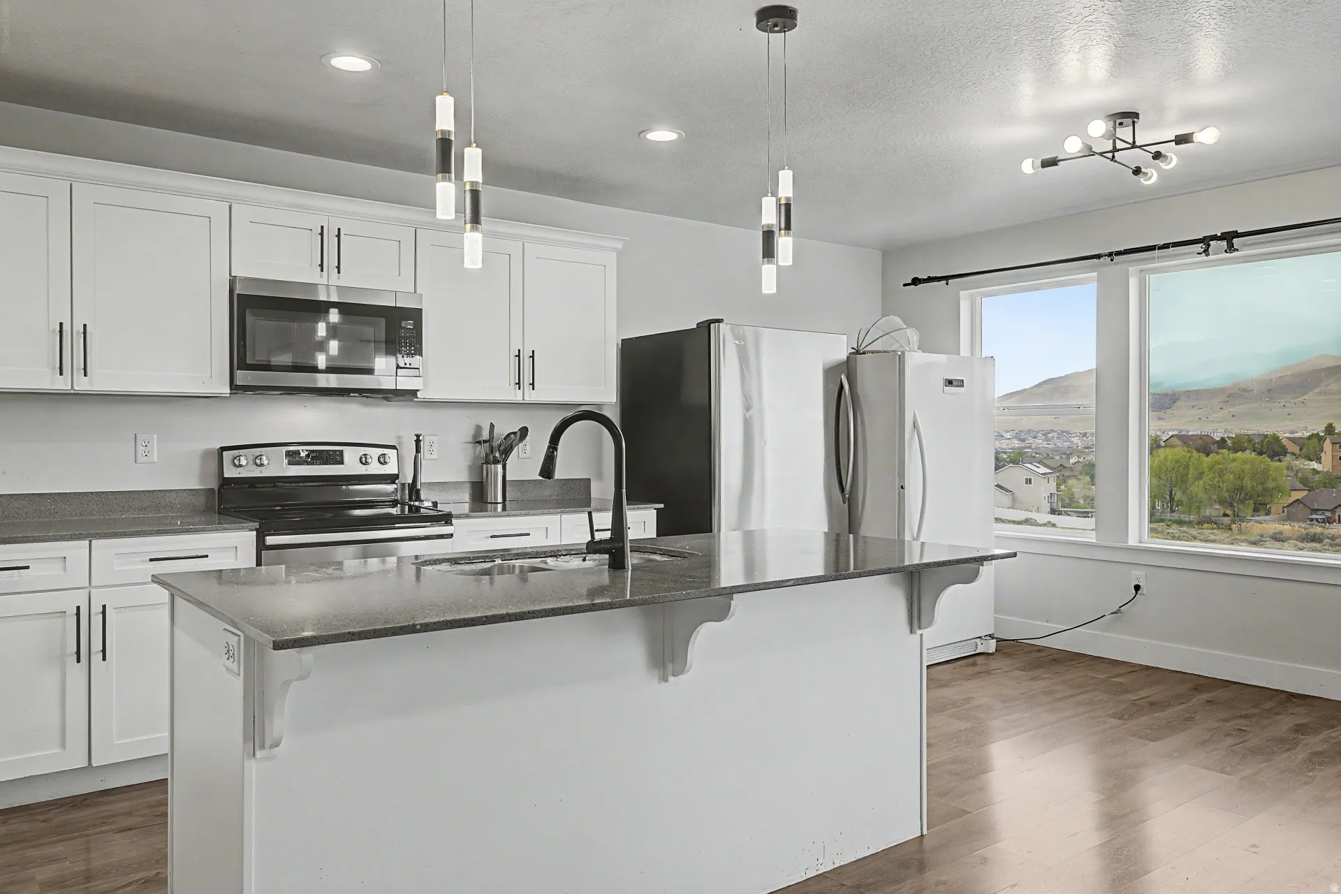 Modern kitchen featuring white cabinetry, a central island with a sink, dark countertops, stainless steel appliances, and wood-finish flooring