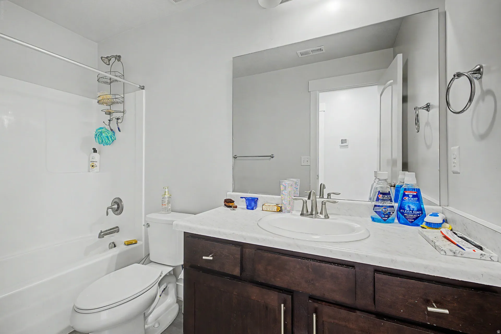 Bathroom featuring a white tub with shower, dark wood-finish vanity with a single basin sink, light countertop, and a large wall-mounted mirror