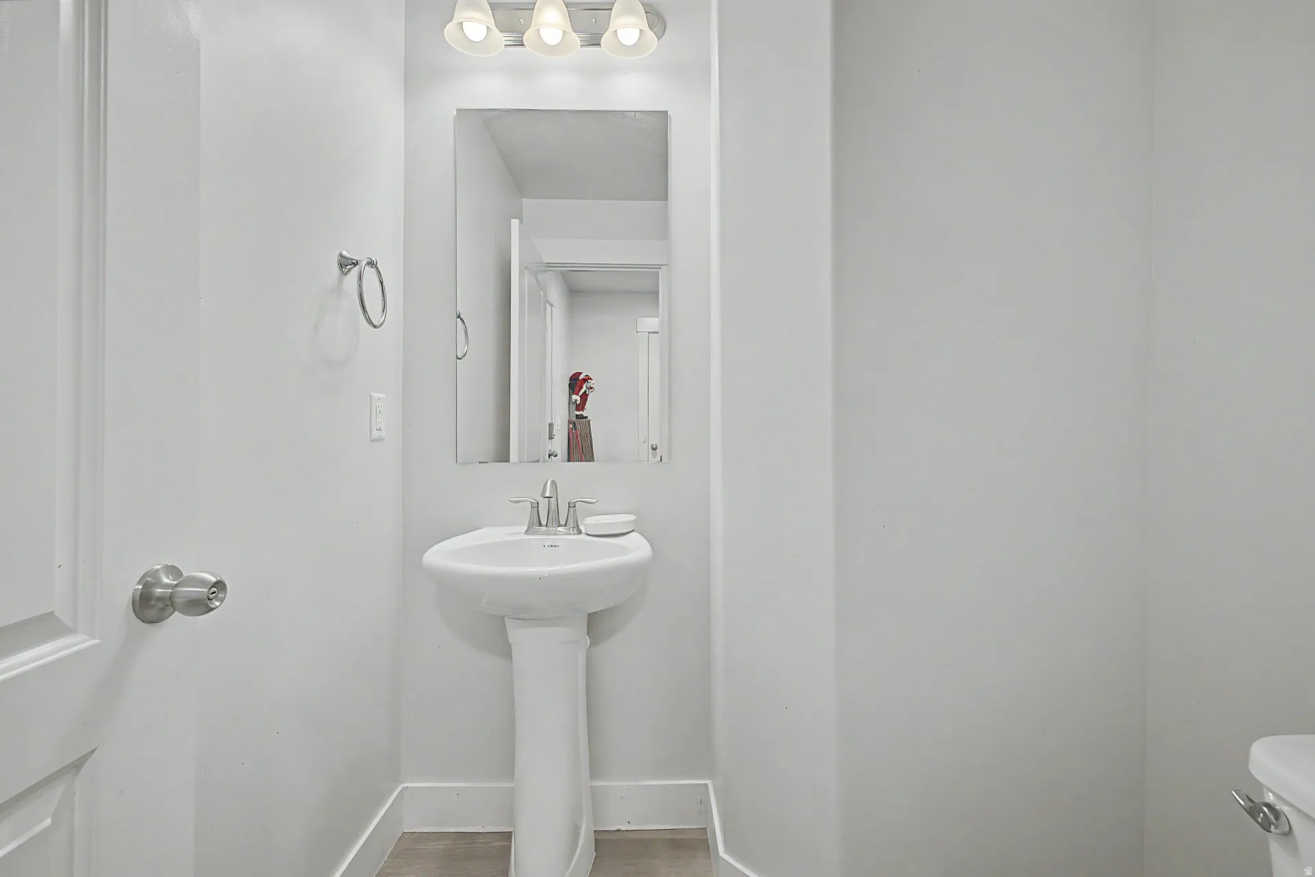 Pedestal sink with chrome faucet, rectangular mirror, and three-bulb vanity light fixture