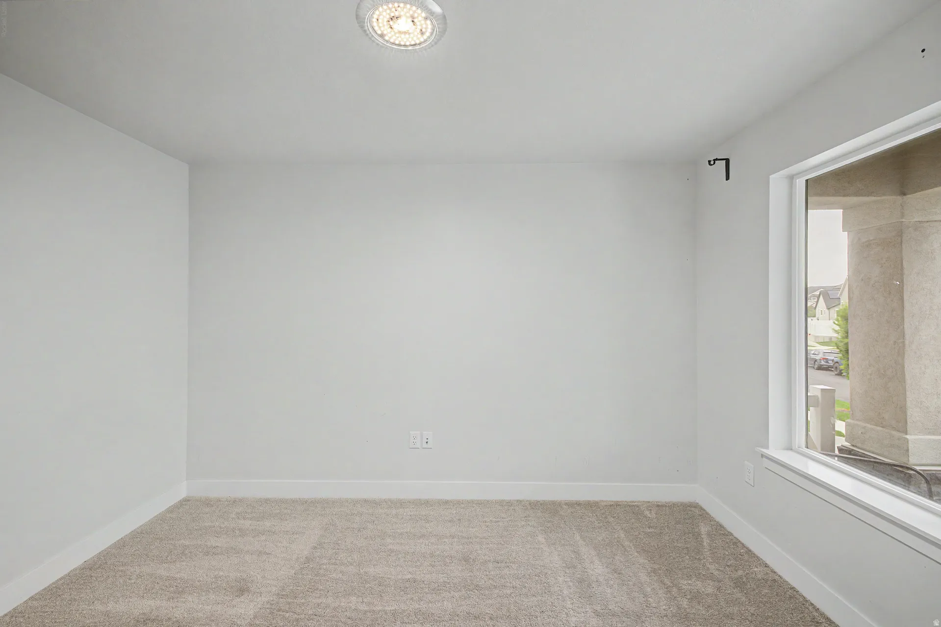 Spacious room featuring neutral carpeting, white baseboards, and a large window with white trim