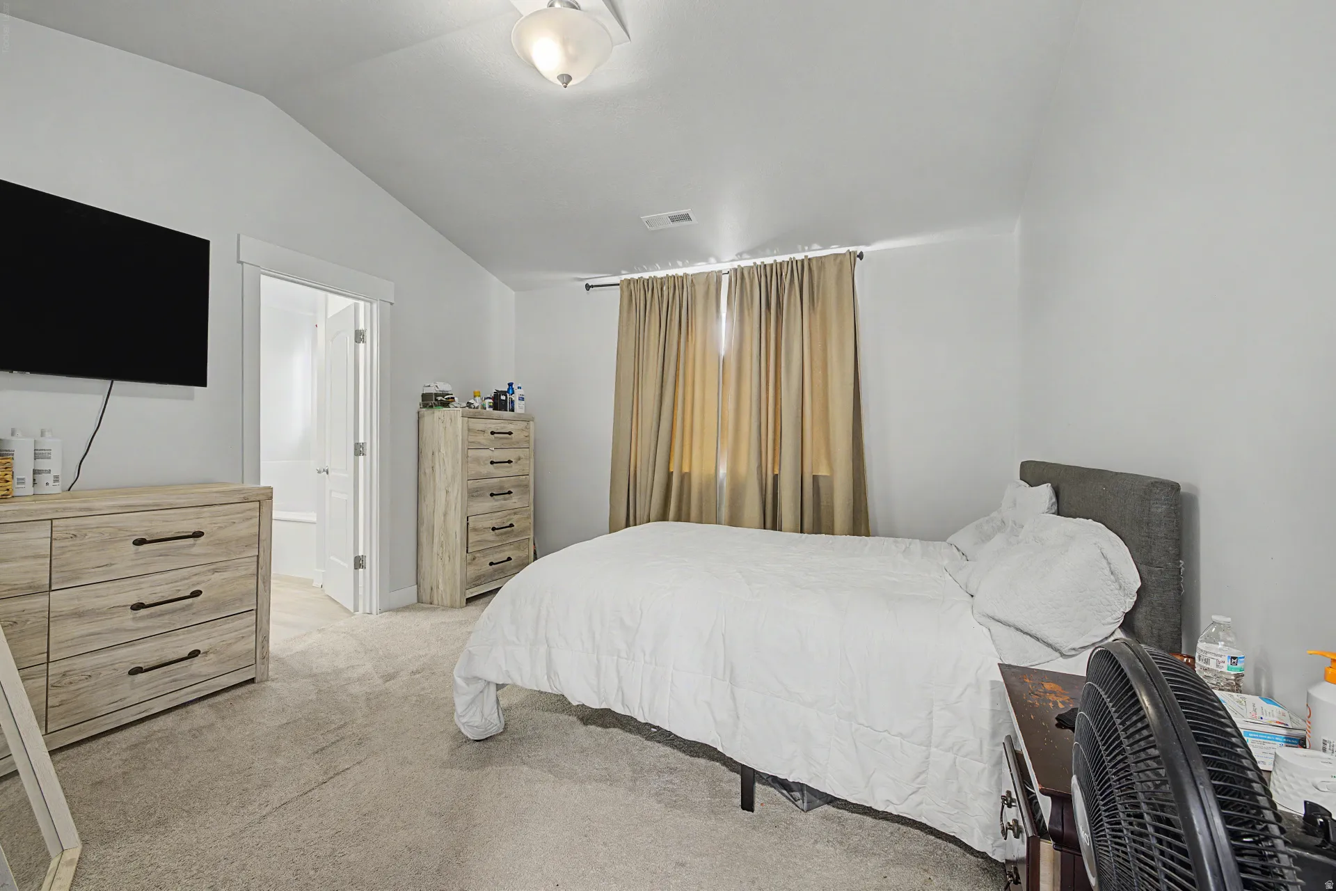Bedroom featuring vaulted ceilings, light-toned carpeting, neutral wall finishes, and a doorway leading to an adjoining bathroom with a visible bathtub
