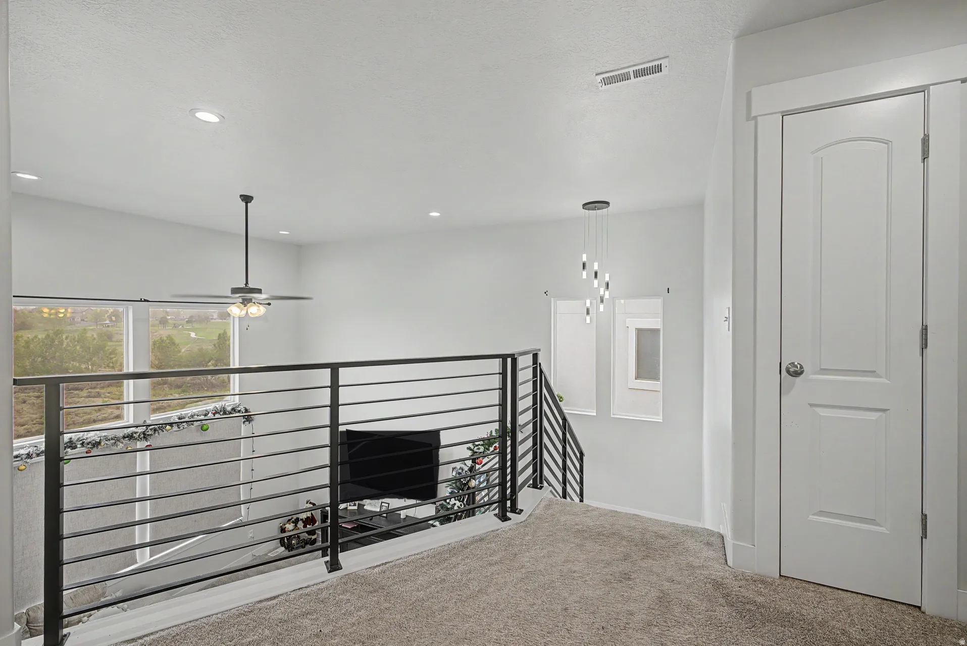 Upper-level landing featuring a contemporary horizontal metal railing, neutral carpet flooring, and a paneled door