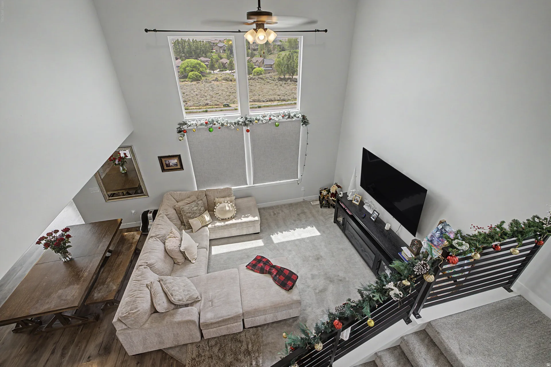 Vaulted ceiling great room featuring expansive windows with roller shades, a ceiling fan, and wood-finish flooring