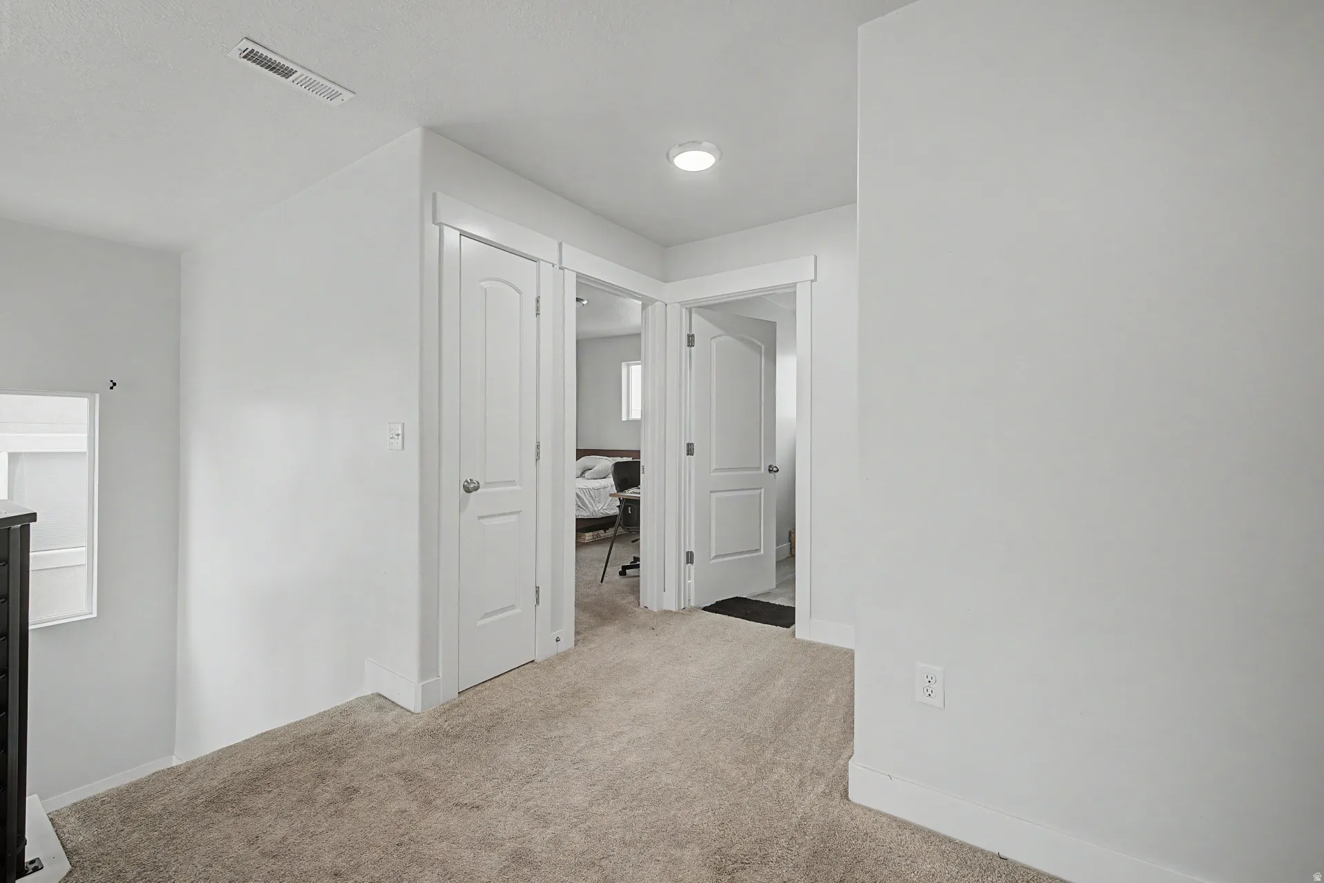 Carpeted hallway with white walls and trim, featuring a recessed ceiling light