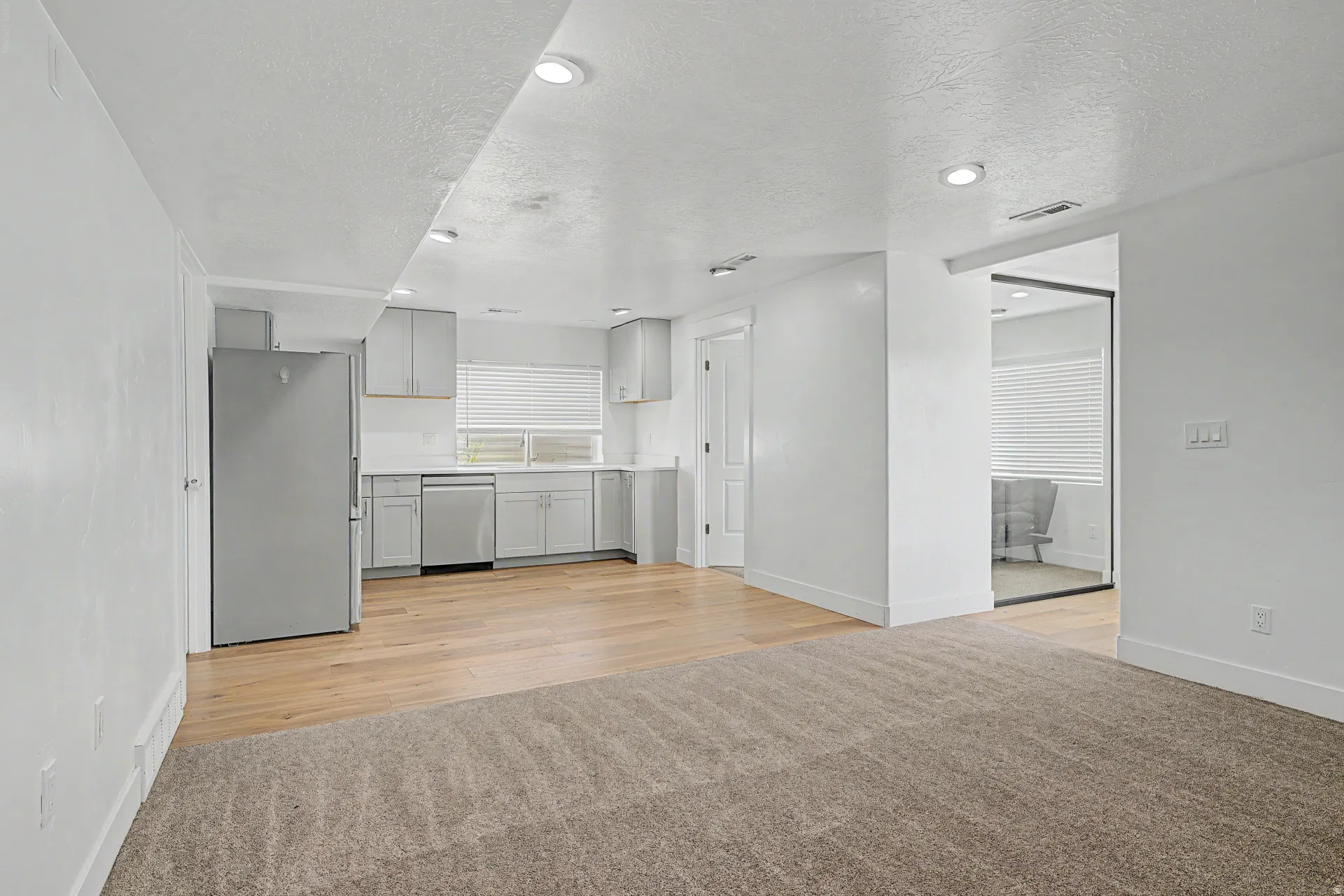 Basement living room Open-concept living area with light-toned wood-finish flooring, recessed lighting, and a modern kitchen featuring stainless steel appliances