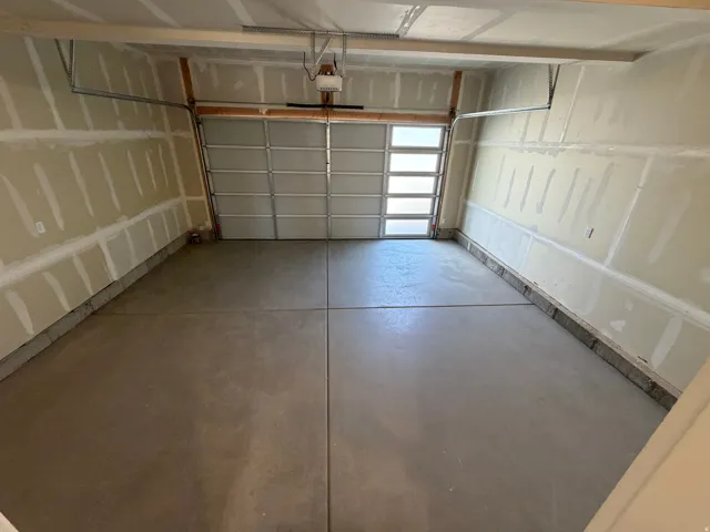 Spacious garage with concrete flooring, automatic garage door opener, and a garage door featuring frosted window panels