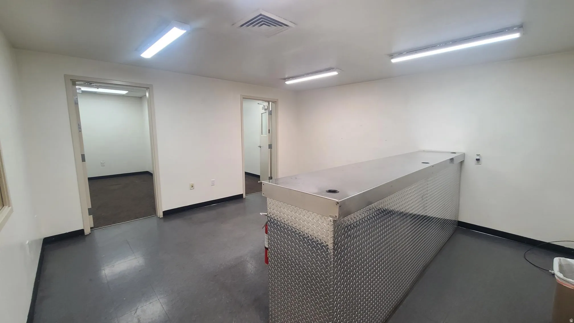 Spacious interior with two open doorways, dark flooring, and a large diamond plate metal counter