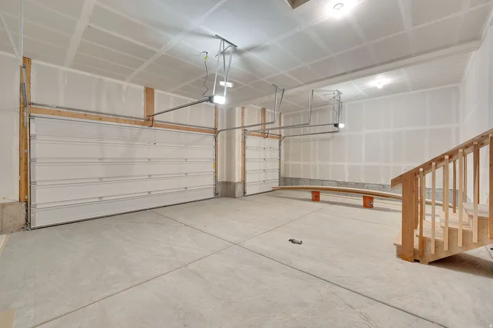 Two-car garage featuring concrete flooring, unpainted drywall, exposed wood framing, and an unfinished wood staircase