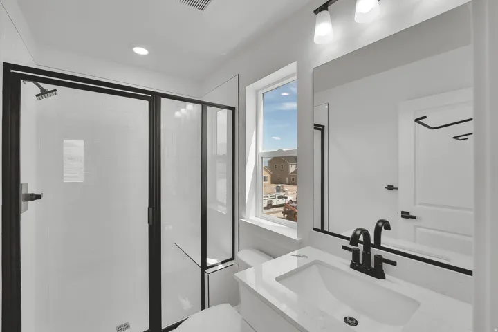 Contemporary bathroom featuring a frameless mirror, white vanity with integrated sink, matte black fixtures, and a shower with black-framed glass enclosure