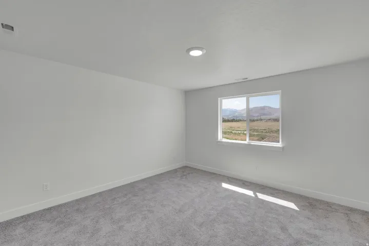 Neutral gray carpeting, white walls, recessed ceiling lighting, a white-framed window, and a mountain backdrop