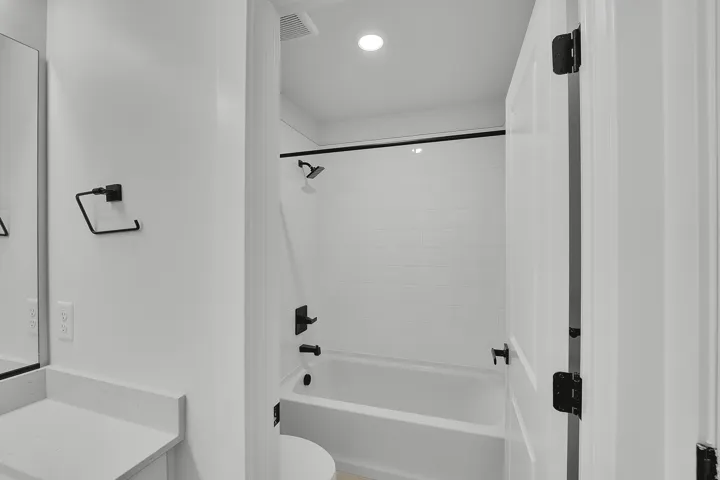 Bathroom featuring a white bathtub with subway tile surround, matte black fixtures, and recessed lighting
