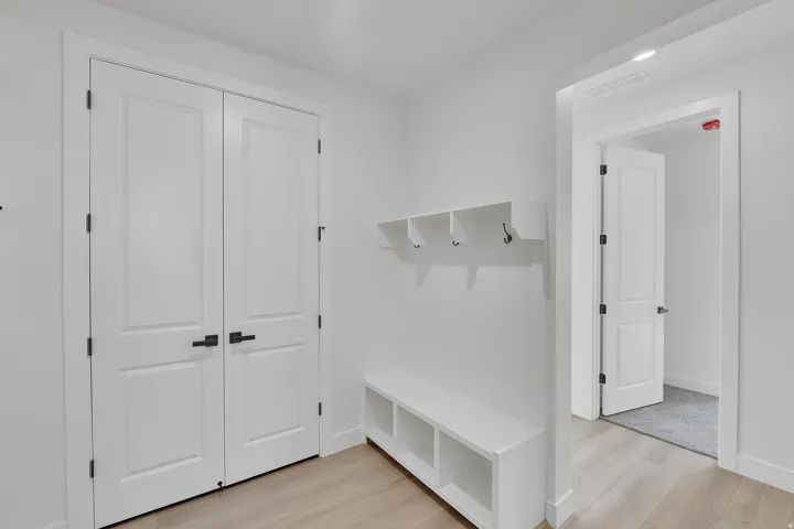 Entryway featuring a built-in bench with storage cubbies, wall-mounted coat hooks, and light wood-finish flooring