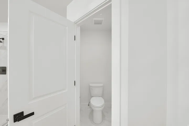 Private water closet featuring white walls, white-finish door, black hardware, and white tile flooring