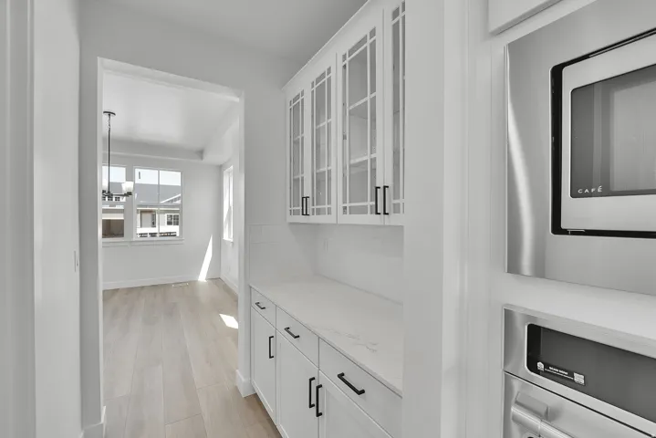 Built-in white cabinetry featuring glass-front uppers, a light-colored countertop, and a tiled backsplash