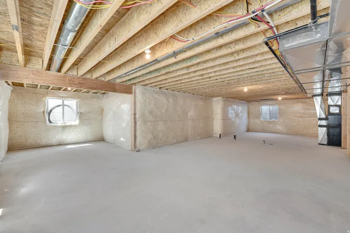 Expansive unfinished basement featuring a concrete floor, exposed wood ceiling joists, and insulated walls