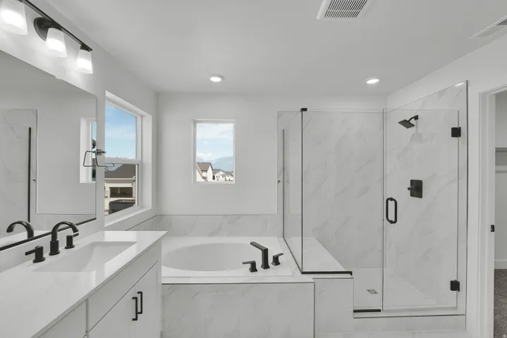 Contemporary bathroom featuring a large soaking tub, glass-enclosed shower with tiled surround, dual vanity with undermount sinks, and matte black fixtures