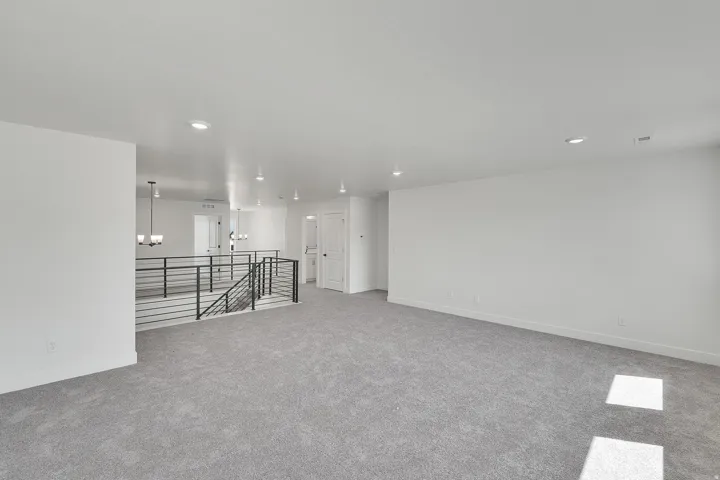 Spacious open loft area featuring plush gray carpeting, recessed ceiling lighting, and a modern horizontal bar railing system