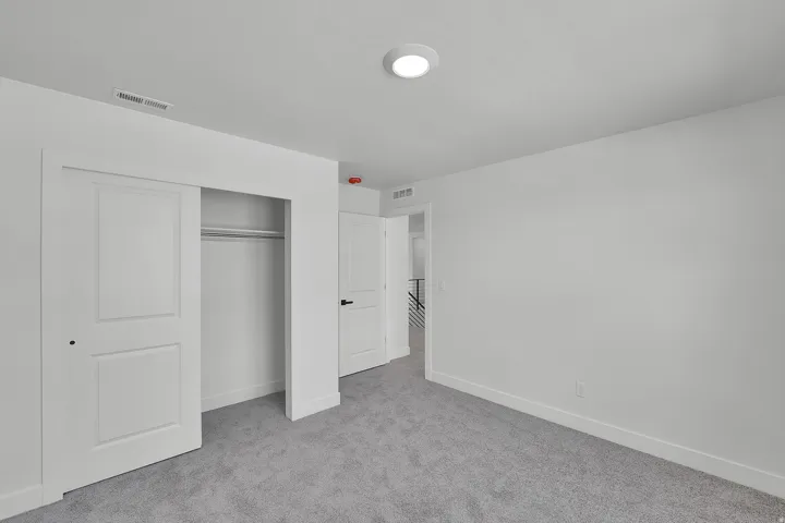 Carpeted room with white walls, a flush-mount ceiling light, and a closet featuring two-panel sliding doors