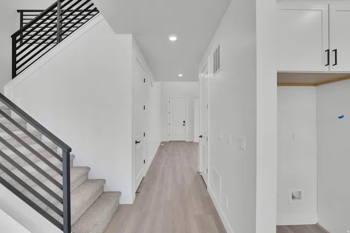 Modern horizontal iron stair railing, light wood-finish flooring, recessed lighting, white shaker cabinetry, and contemporary black hardware