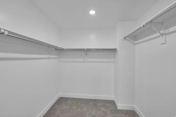 Walk-in closet featuring light gray carpet, white baseboards, multiple chrome hanging rods, and recessed ceiling lighting