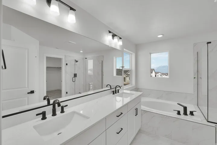 Spacious bathroom featuring a dual vanity with white cabinetry and quartz countertops, matte black fixtures, an oversized soaking tub, and a glass-enclosed shower with tiled walls