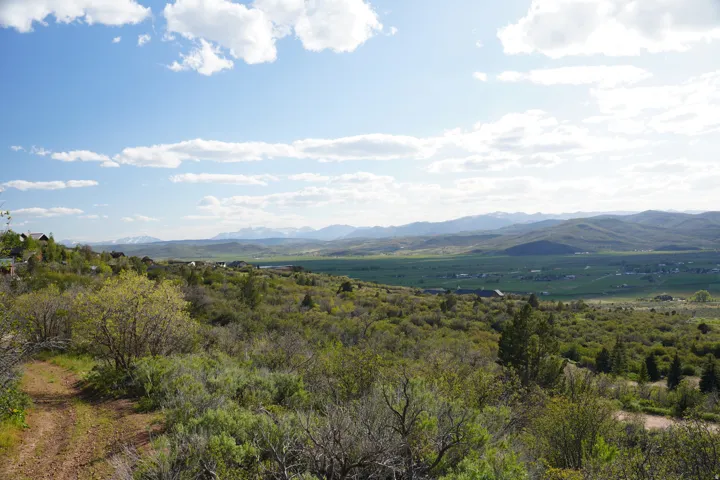 Expansive mountain landscape featuring a broad valley, distant peaks, and scattered residential structures