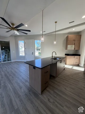Kitchen island with a black countertop, wood-finish cabinetry, and an integrated sink