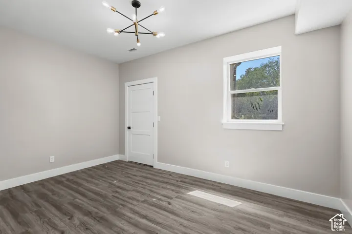Spacious room featuring wood-finish flooring, light gray wall tones, a modern sputnik chandelier, white trim, and a white interior door