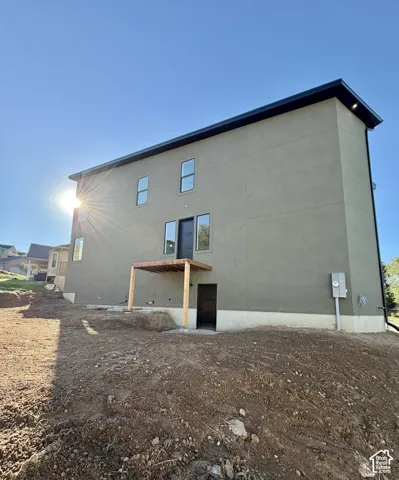 Stucco exterior with a flat roofline, featuring multiple windows, a dark framed door, and a partially constructed wooden patio cover