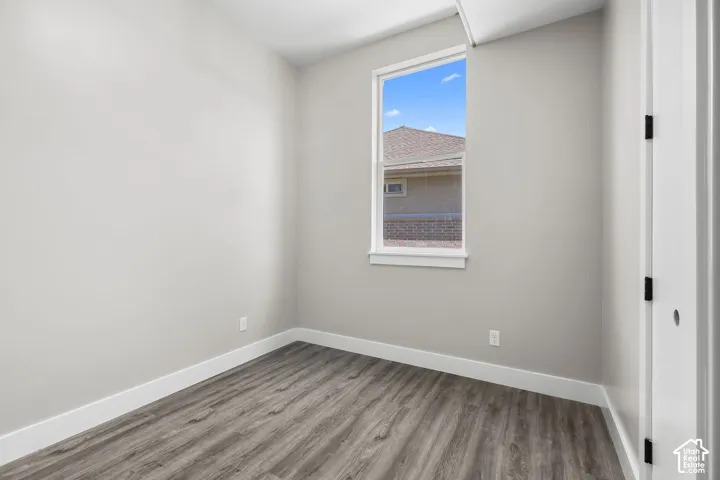 Light-filled room featuring a single window, wood-finish flooring, light grey walls, white baseboards, and a white door with black hardware