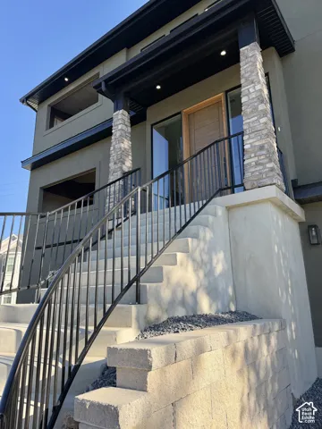 Stone veneer columns accenting the entry, a prominent wooden entry door, recessed soffit lighting, and curved metal railings