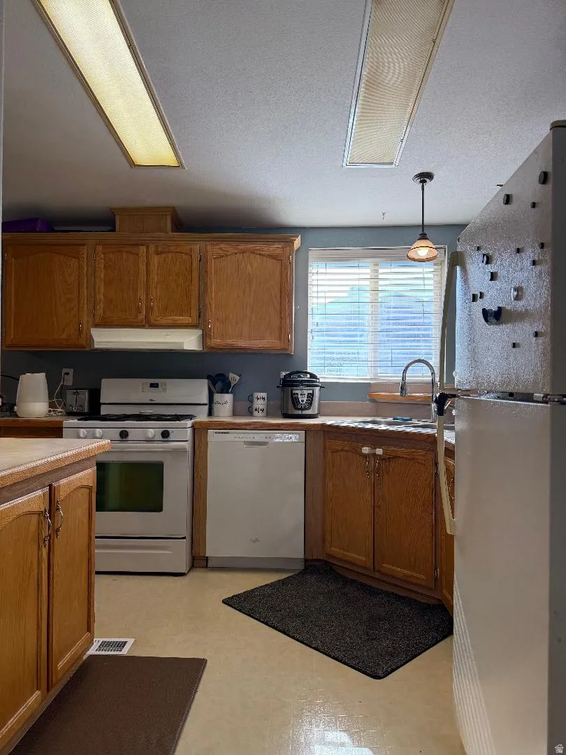 Kitchen featuring wood cabinetry, a window with horizontal blinds, a built-in dishwasher, and a white oven with a stovetop