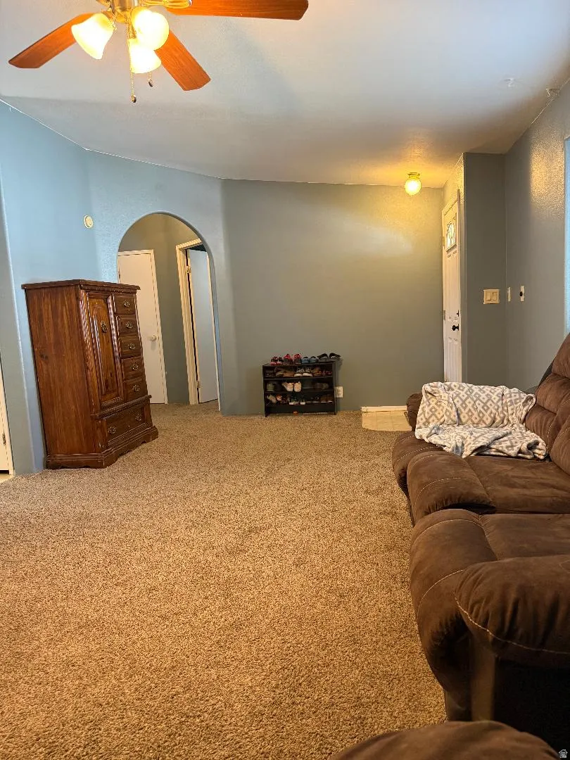 Carpeted living area featuring a ceiling fan with light fixture, arched doorway, and light blue wall paint