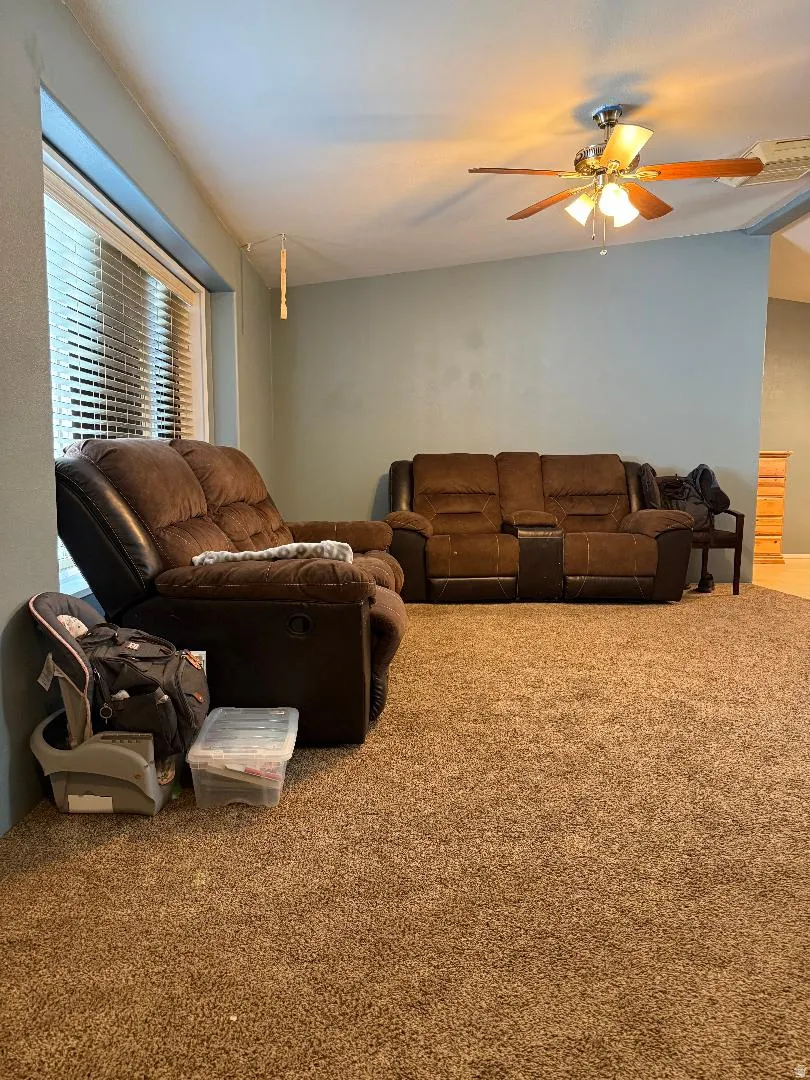 Carpeted living area featuring a ceiling fan with integrated lighting, a window with horizontal blinds, and light-toned wall paint