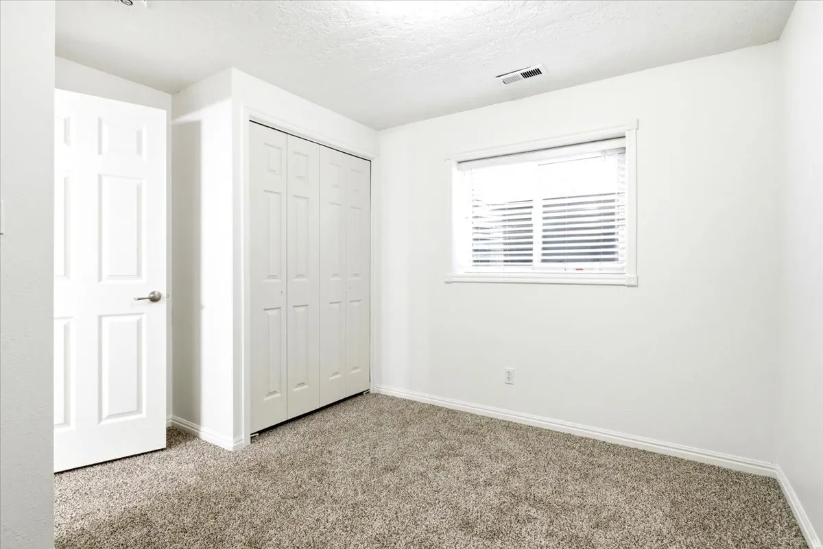 Room featuring plush gray carpeting, a window with blinds, a white paneled door, and a bi-fold closet