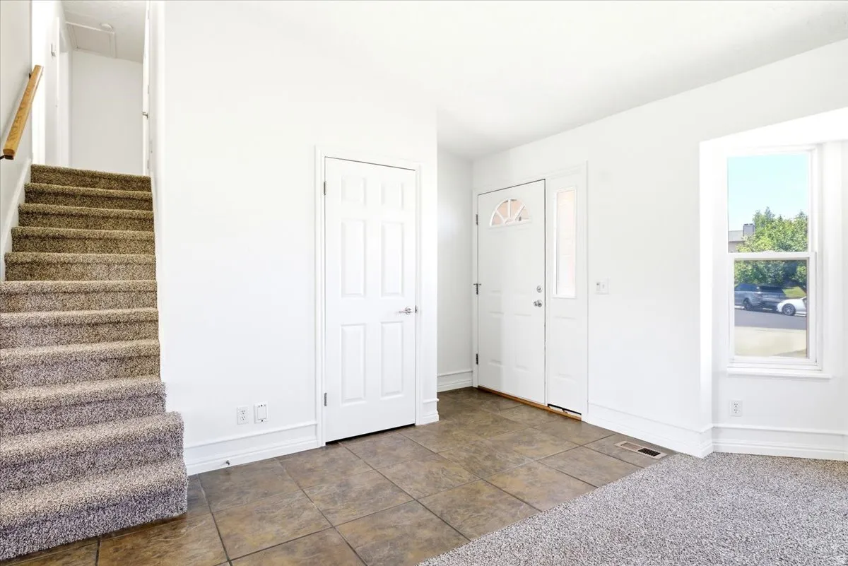 Foyer featuring tiled flooring, a paneled entry door with sidelight, a double-hung window, a carpeted staircase with a wood handrail, and white baseboards