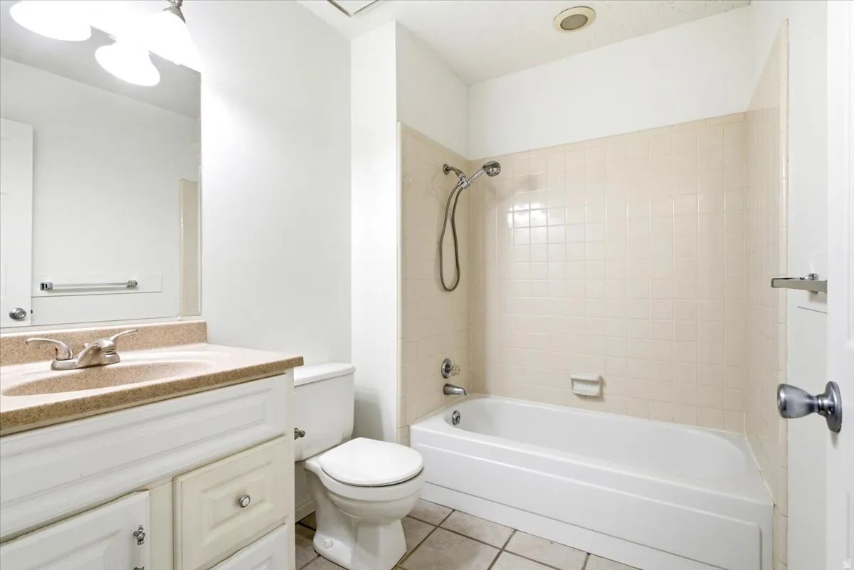 Bathroom featuring a white vanity with a light-toned countertop, a matching toilet, and a white bathtub with a tiled surround