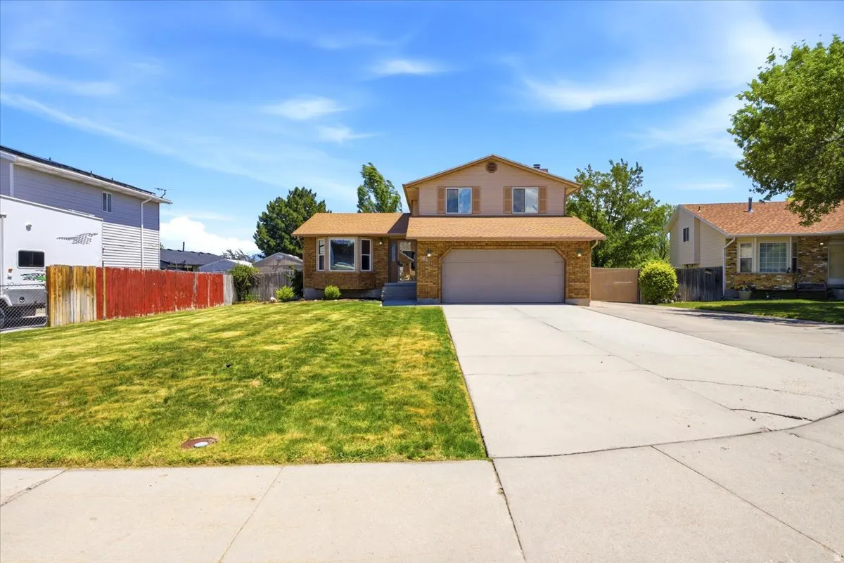 Brick and siding exterior with a two-car garage, mature front lawn, concrete driveway, and established landscaping